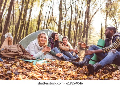 Young friends travelers sitting and talking near tent in autumn forest
