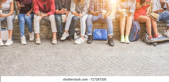 Young friends using smartphones and drinking coffee outdoor - Group of people having fun with technology trends - Youth, new generation addiction and friendship concept - Main focus on center guys - Shutterstock ID 717187105