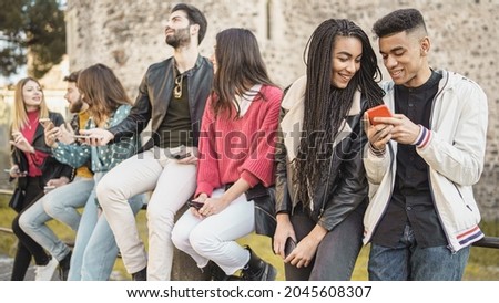 young friends watching viral social media video on mobile cell phone outdoors - Young adult friends using smartphones together -outdoors youth culture concept

