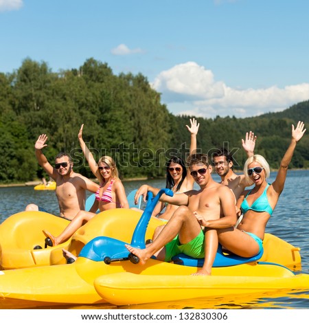 Young friends waving from pedal boats on lake summer vacation