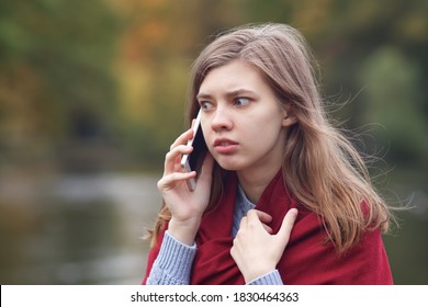 Young frightened scared angry woman talking on her cell mobile smart phone, having negative call, conversation outdoors in park, feeling nervous
