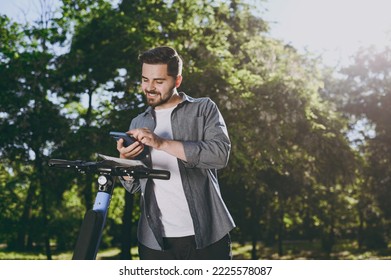 Young front bottom view smiling man 20s wearing blue shirt riding scooter using mobile cell phone browsing route go down alley rest in spring green city park outdoors on nature Urban leisure concept - Powered by Shutterstock