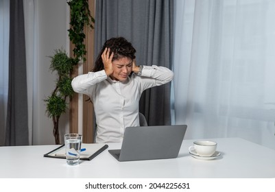 Young frustrated businesswoman is sitting in the home office cover her ears with her hands working on a laptop and is angry about the loud noise made by the workers upstairs because she can't work - Powered by Shutterstock