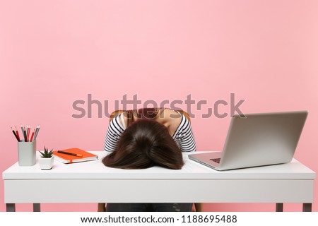 Young frustrated exhausted woman laid her head down on the table sit work at white desk with contemporary pc laptop isolated on pastel pink background. Achievement business career concept. Copy space