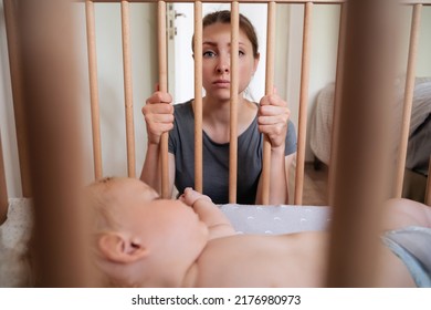 Young frustrated mother feels imprison while takes care of her infant and suffering from postnatal depression. Depressed woman looking at camera while her little toddler baby sleeping in his bed