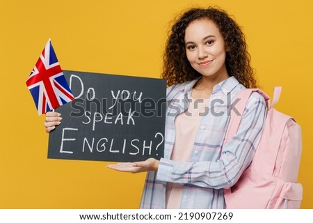 Young fun black teen girl student she wear casual clothes backpack bag hold british flag card sign do you speak english title text isolated on plain yellow background. High school university concept