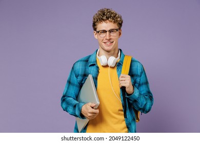 Young Fun Boy Teen Student In Casual Clothes Backpack Headphones Glasses Hold Closed Laptop Pc Computer Isolated On Plain Violet Background Studio. Education In High School University College Concept