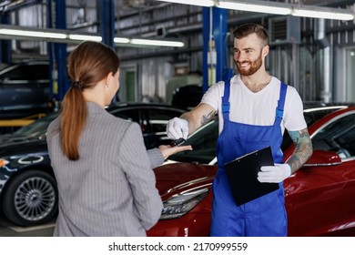 Young fun car mechanic man in denim blue overalls white t-shirt gloves hold clipboard with papers document talk with female driver owner give keys work in modern vehicle repair shop workshop indoors. - Powered by Shutterstock