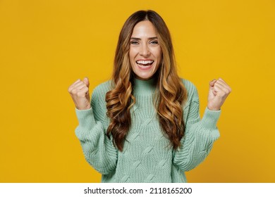 Young fun caucasian woman 30s wearing green knitted sweater doing winner gesture celebrate clenching fists say yes isolated on plain yellow color background studio portrait. People lifestyle concept
