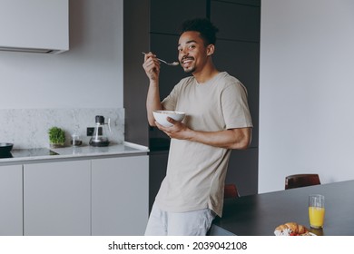 Young fun cheerful smiling african american man in casual clothes eat breakfast muesli cereals with milk fruit in bowl prepare cook food in light kitchen at home alone indoor. Healthy diet concept. - Powered by Shutterstock