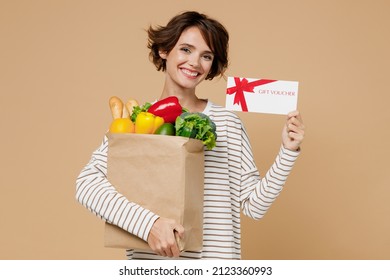 Young Fun Cheerful Vegetarian Woman 20s In Casual Clothes Hold Paper Bag With Vegetables Hold Gift Certificate Coupon Voucher Card For Store Isolated On Plain Pastel Beige Background Shopping Concept