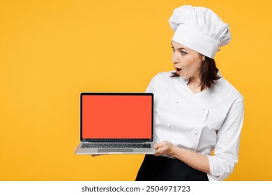 Young fun chef cook baker woman wear white shirt black apron uniform toque chefs hat hold use blank screen laptop pc computer look for recipe isolated on plain yellow background. Cooking food concept - Powered by Shutterstock