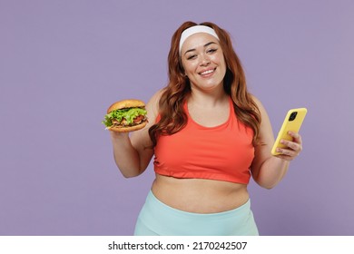 Young Fun Chubby Overweight Plus Size Big Fat Fit Woman In Red Top Warm Up Training Hold Fast Food Burger Mobile Cell Phone App Counts Calories Isolated On Purple Background Gym Workout Sport Concept