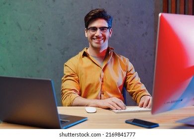 Young Fun Confident Employee Programmer IT Specialist Business Man In Casual Shirt Sit Work At Office Desk With Pc Laptop Desktop Computer Writing Code Achievement Career Program Development Concept