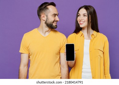 Young Fun Cool Couple Two Friends Family Man Woman Together In Yellow Clothes Hold In Hand Use Mobile Cell Phone With Blank Screen Workspace Area Look To Each Other Isolated On Plain Violet Background