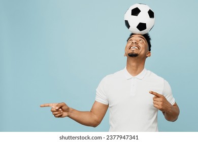 Young fun cool man fan wearing basic t-shirt cheer up support football sport team holding in hand soccer ball on head point aside watch tv live stream isolated on plain pastel blue color background - Powered by Shutterstock