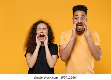 Young fun couple two american friends together family informer man african woman 20s wearing yellow black t-shirt scream news with hands near mouth isolated on orange color background studio portrait