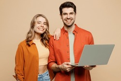Young Fun Couple Two Friends Family IT Man Woman Wear Casual Clothes Looking Camera Hold Use Work On Laptop Pc Computer Together Isolated On Pastel Plain Light Beige Color Background Studio Portrait