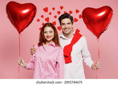 Young fun couple two friends woman man wear shirt hold red bunch of inflatable balloons look camera isolated on plain pink background studio portrait. Valentine's Day birthday holiday party concept