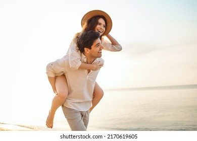 Young fun couple two friends family man woman in white clothes boyfriend give piggyback ride to joyful, girlfriend sit on back at sunrise over sea beach ocean outdoor seaside in summer day white sky - Powered by Shutterstock