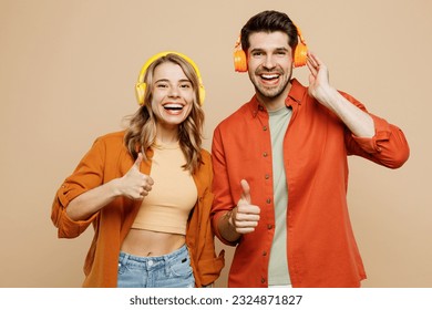 Young fun couple two friends family man woman wear casual clothes headphones listen music show thumb up looking camera together isolated on pastel plain light beige color background studio portrait - Powered by Shutterstock