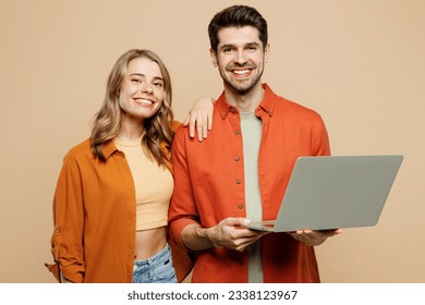 Young fun couple two friends family IT man woman wear casual clothes looking camera hold use work on laptop pc computer together isolated on pastel plain light beige color background studio portrait - Shutterstock ID 2338123967