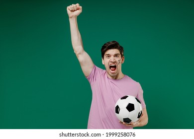 Young fun crazy european man fan wear basic pink t-shirt cheer up support football sport team hold soccer ball watch tv live stream scream raised hand up isolated on dark green color background studio