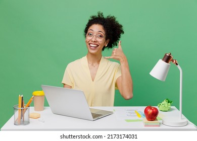 Young Fun Employee Business Woman Of African American Ethnicity Wear Shirt Sit Work At White Office Desk With Pc Laptop Doing Phone Gesture Like Says Call Me Back Isolated On Plain Green Background.