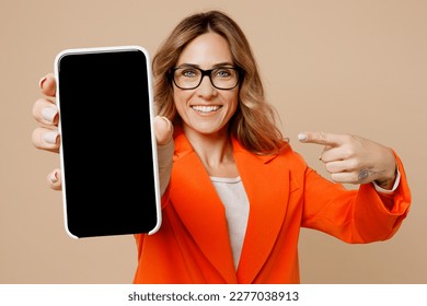 Young fun employee business woman corporate lawyer wear classic formal orange suit glasses work in office hold use mobile cell phone show blank screen workspace area isolated on plain beige background
