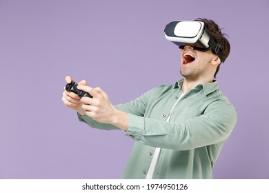 Young fun excited amazed man 20s wear casual green mint shirt white t-shirt playing pc game with joystick console watching in vr headset pc gadget isolated on purple color background studio portrait
