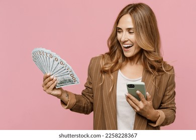 Young fun excited exultant employee business woman 30s she wear casual classic jacket hold mobile cell phone fan of cash money in dollar banknotes isolated on plain pastel light pink background studio - Shutterstock ID 2258228367