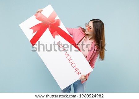 Young fun excited happy overjoyed caucasian woman 20s wearing pastel pink clothes glasses hold large huge gift voucher flyer mock up isolated on blue color background studio People lifestyle concept