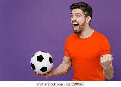 Young fun exultant happy fan man he 20s wearing orange t-shirt cheer up support football sport team hold in hand soccer ball watch tv live stream do winner gesture isolated on plain purple background - Shutterstock ID 2203299893