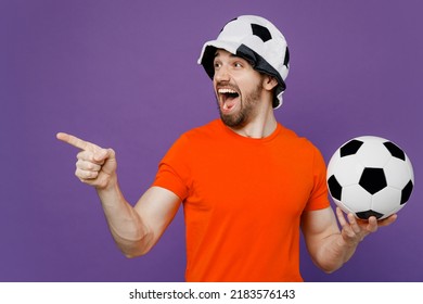 Young Fun Fan Man Wear Orange T-shirt He Cheer Up Support Football Sport Team Hold Soccer Ball Panama Hat Watch Tv Live Stream Point Index Finger Aside On Workspace Isolated On Plain Purple Background