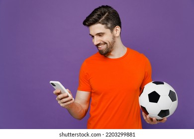 Young fun fan smiling happy man he wear orange t-shirt cheer up support football sport team hold in hand soccer ball watch tv live stream 2024 use mobile cell phone isolated on plain purple background - Shutterstock ID 2203299881