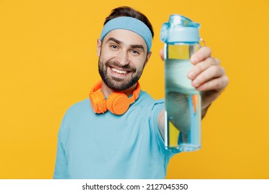 Young Fun Fitness Trainer Instructor Sporty Man Sportsman In Headband Blue T-shirt Spend Weekend In Home Gym Give Bottle Of Water Isolated On Plain Yellow Background. Workout Sport Motivation Concept