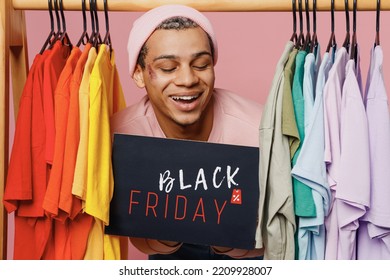 Young Fun Gay Man Wear Sweatshirt Hat Hold Card Sign With Black Friday Title Text Near Rack With T-shirts At Store Isolated On Plain Pastel Light Pink Background Studio. Lifestyle Lgbtq Pride Concept