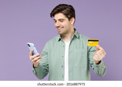 Young Fun Happy Caucasian Man 20s Wear Casual Mint Shirt White T-shirt Hold Mobile Cell Phone Credit Bank Card Shopping Online Isolated On Purple Background Studio Portrait People Lifestyle Concept