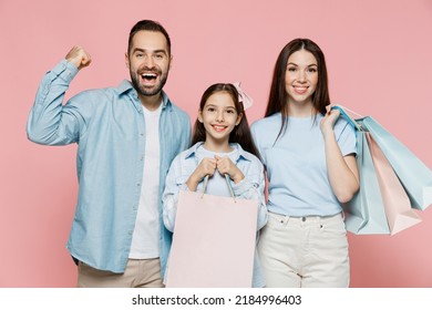 Young Fun Happy Parents Mom Dad With Child Kid Daughter Teen Girl In Blue Clothes Holding Package Bags With Purchases After Shopping Do Winner Gesture Isolated On Plain Pastel Light Pink Background.