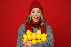Young Fun Happy Woman Wear Grey Sweater Scarf Hat Hold In Hands Lot Of Lemon Fruits C Isolated On Plain Red Background Studio Portrait. Healthy Lifestyle Ill Sick Disease Treatment Cold Season Concept