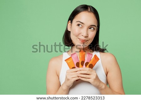 Young fun happy woman wear white clothes hold in hand many protein bars look aside on area isolated on plain pastel light green background. Proper nutrition healthy fast food unhealthy choice concept