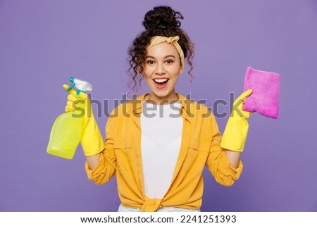 Young fun housekeeper woman wear yellow shirt tidy up hold in hand bottle use spray detergent cleanser rag microfiber cloth isolated on plain pastel light purple background studio. Housework concept Imagine de stoc © 