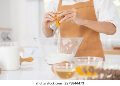 Young fun housewife housekeeper chef baker woman in light brown apron work at table kitchenware cracking an egg baking cake in kitchen .Process cooking food concept  Woman baking at home. - Powered by Shutterstock