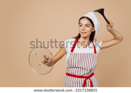 Young fun housewife housekeeper chef baker latin woman wear striped apron toque hat hold pan lid pov fencing fighting fooling around isolated on plain pastel light beige background. Cook food concept