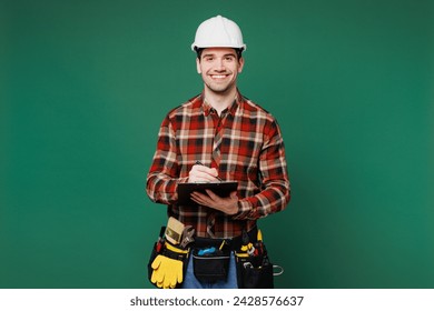 Young fun laborer man wear red shirt hardhat hat work write in clipboard with paper documents isolated on plain green background. Instruments accessories for renovation apartment. Repair home concept - Powered by Shutterstock