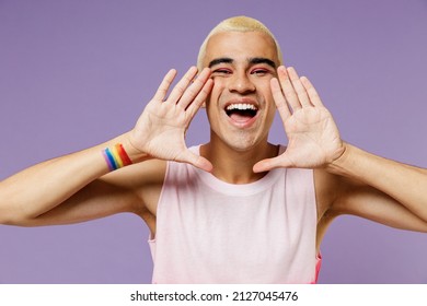 Young fun latin gay man with make up wear bright pink top hold hands near mouth speak shout scream coming out isolated on plain pastel purple background studio People lifestyle fashion lgbtq concept