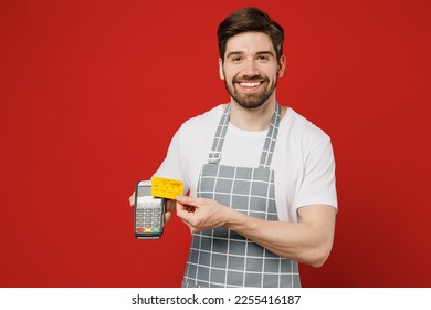 Young fun male housewife housekeeper chef cook baker man wear grey apron hold wireless modern bank payment terminal to process acquire credit card isolated on plain red background Cooking food concept - Shutterstock ID 2255416187