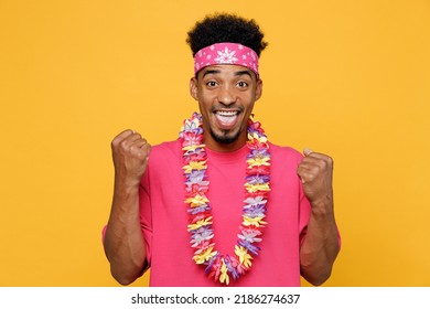 Young Fun Man 20s He Wear Pink T-shirt Hawaiian Lei Bandana Near Hotel Pool Doing Winner Gesture Celebrate Clenching Fists Say Yes Isolated On Plain Yellow Background. Summer Vacation Sea Rest Concept