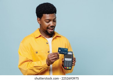 Young fun man of African American ethnicity 20s in yellow shirt hold wireless modern bank payment terminal to process acquire credit card payments isolated on plain pastel light blue background studio - Shutterstock ID 2252693975