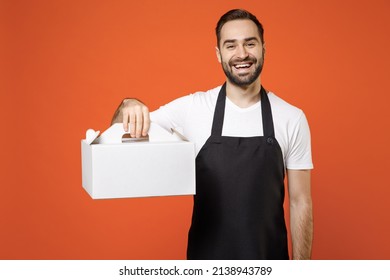 Young Fun Man Barista Bartender Barman Employee In Apron White T-shirt Work In Coffee Shop Clear Blank Craft Paper Takeaway Cake Bag Isolated On Orange Background Studio Small Business Startup Concept